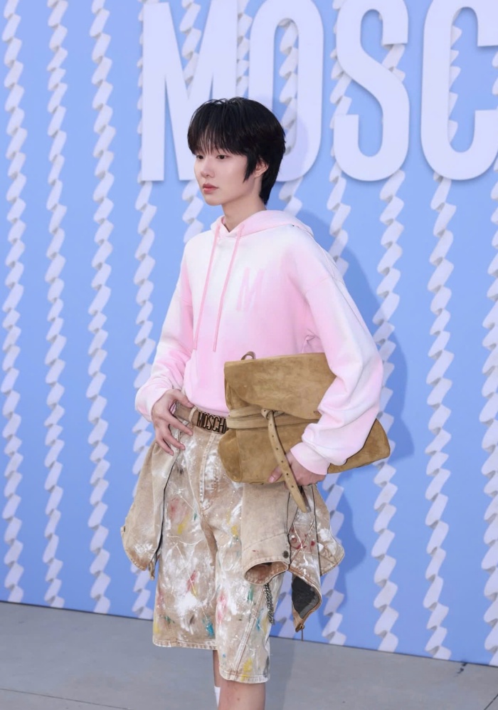 Tại khu vực check-in show của Moschino, Nam Ping xuất hiện với chiếc áo hoodie màu hồng pastel kết hợp quần short họa tiết loang sơn. Trang phục mang tinh thần “workwear nghệ thuật” được nhiều nhà mốt khai thác tại Milan Fashion Week năm nay. Anh chàng mang kèm chiếc túi da nâu dáng gập cùng thắt lưng bản lớn giúp tổng thể outfit càng “chất chơi”.