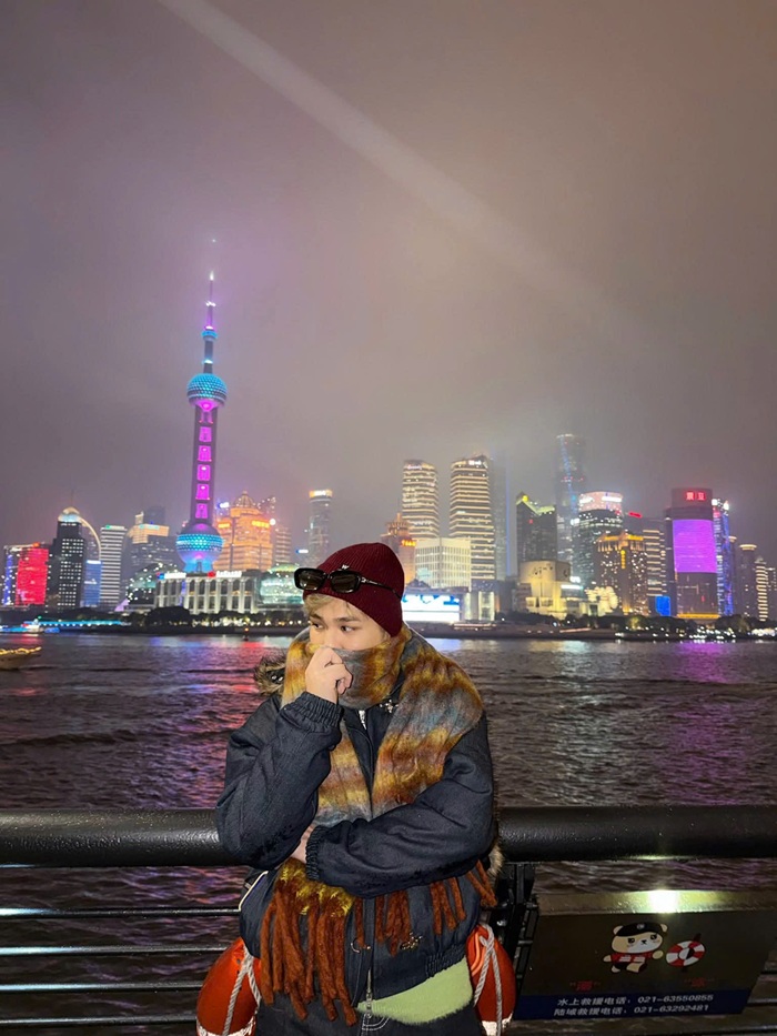 Captain Boy tạo dáng bên bờ sông, phía xa là toàn cảnh Thượng Hải về đêm rực rỡ ánh đèn. Ảnh: FBNV