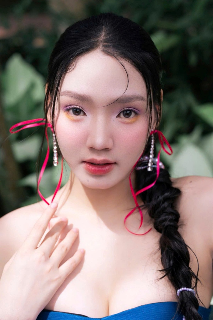 Đôi bông tai tua rua đỏ dài rực rỡ không chỉ phù hợp với không khí Tết mà còn giúp gương mặt thêm phần bừng sáng và thu hút giữa bối cảnh thiên nhiên xanh mướt.