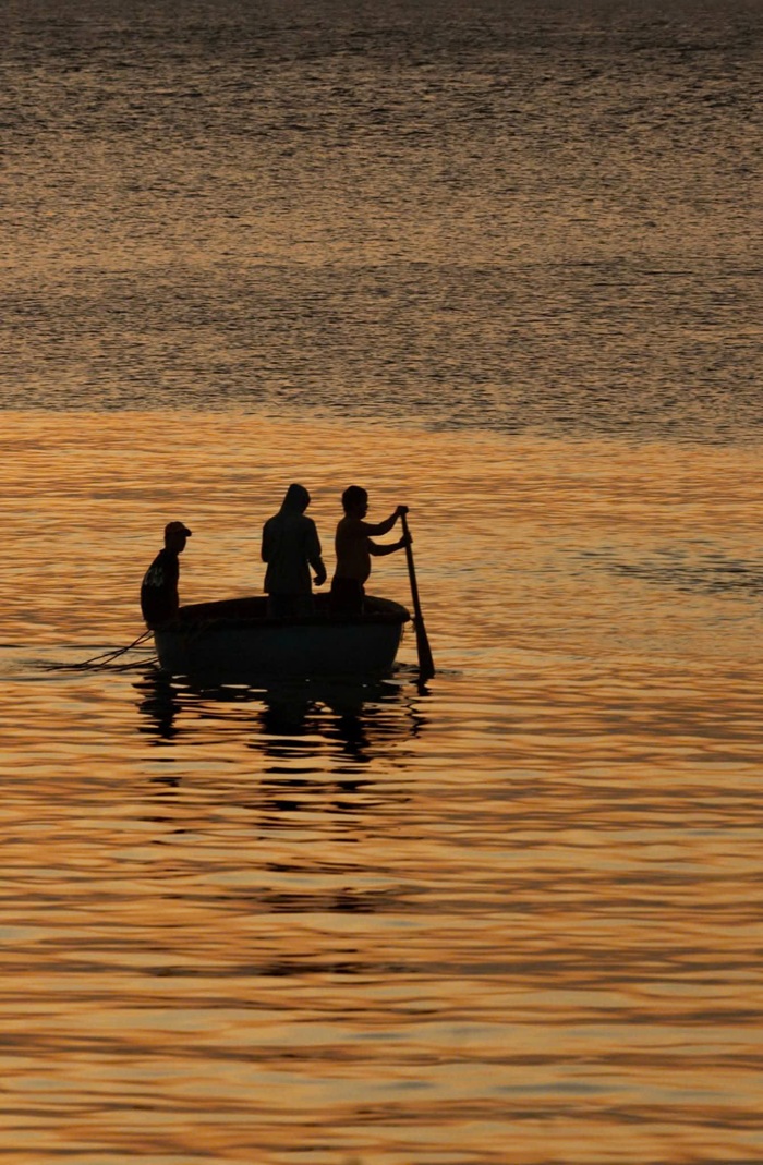 Chiếc thuyền thúng nhỏ của ngư dân lặng lẽ trôi trên mặt nước, bóng người in đậm trên nền hoàng hôn. Ảnh: Tuấn Thành