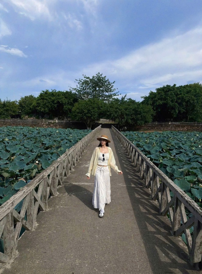 Chuyển sang một khoảnh khắc khác, cô nàng như hòa mình vào với thiên nhiên xứ Huế qua hình ảnh đầm sen trải dài mênh mông. Bước đi trên cây cầu nhỏ giữa lòng đầm, Trương Quỳnh Anh hiện lên như một nàng thơ giữa khung cảnh hữu tình. Những lá sen xanh mướt, điểm xuyết chút sắc trắng tinh khôi của hoa tạo nên một bức tranh vừa bình yên, vừa thơ mộng. 